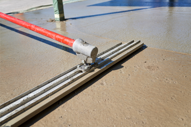 Worker screeding cement floor with bull float